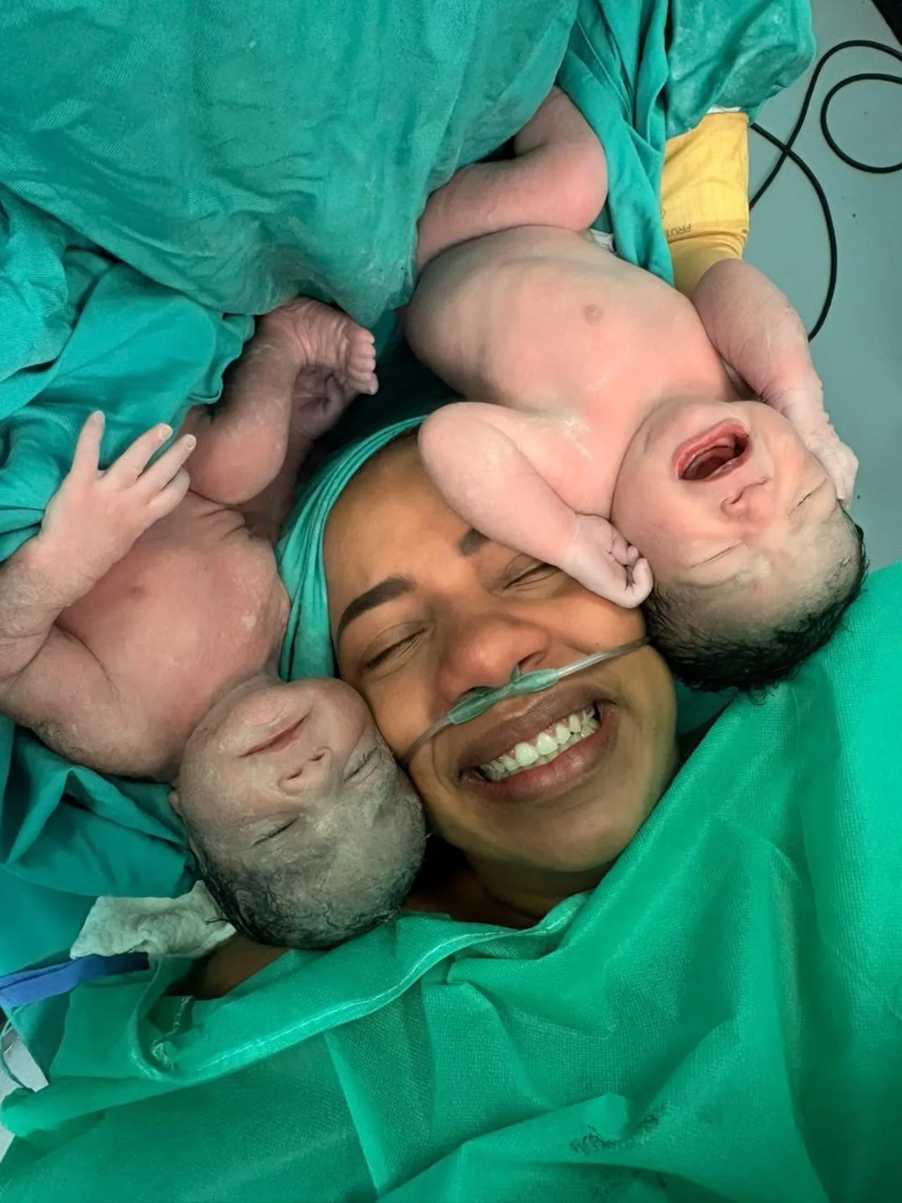 Una madre sonríe junto a sus gemelos recién nacidos